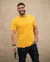 man in yellow crew neck t-shirt and black denim jeans standing beside white wall